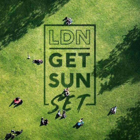 An overhead shot of a sunny park with people sitting on the grass. In the centre on the grass is written LDN Get Sun Set