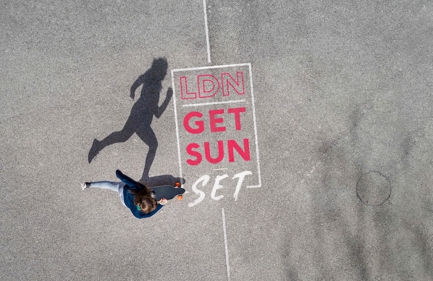 A overhead shot of a skater on concrete. On the concrete is written the words LDN Get Sun Set.
