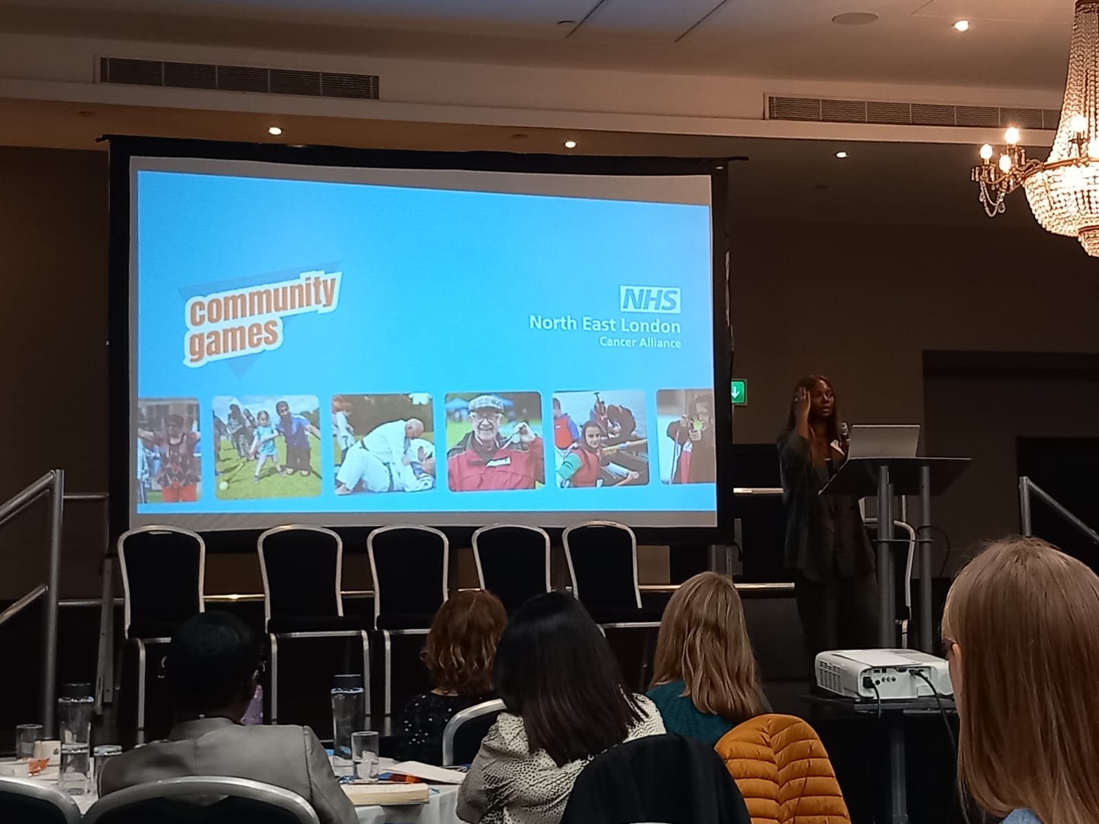 A woman is standing on stage in front of a large screen giving a presentation.