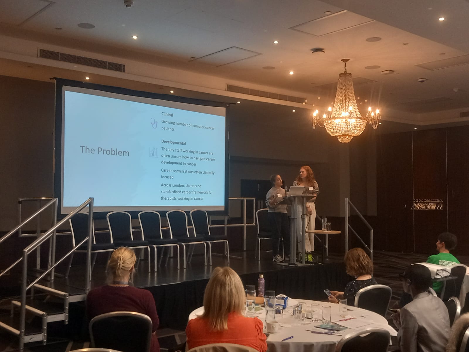 Two women are standing on stage giving a presentation in front of a large screen.