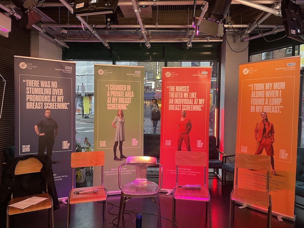 An image of four different coloured posters on a stage with messages about attending breast screening on them.