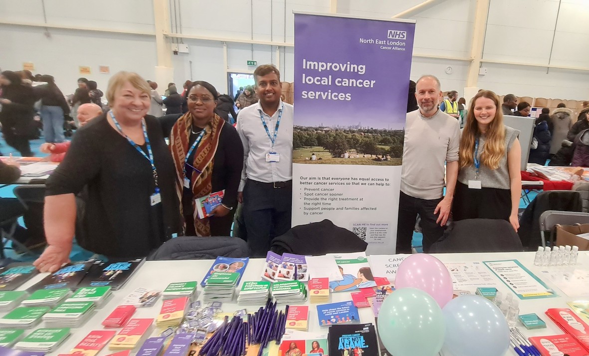 A group of people are standing behind a cancer awareness stand which has cancer information leaflets on it