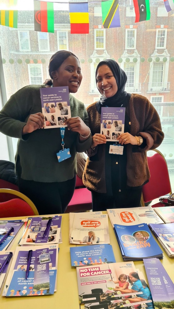 Two women are standing behind a table with cancer information leaflets on it