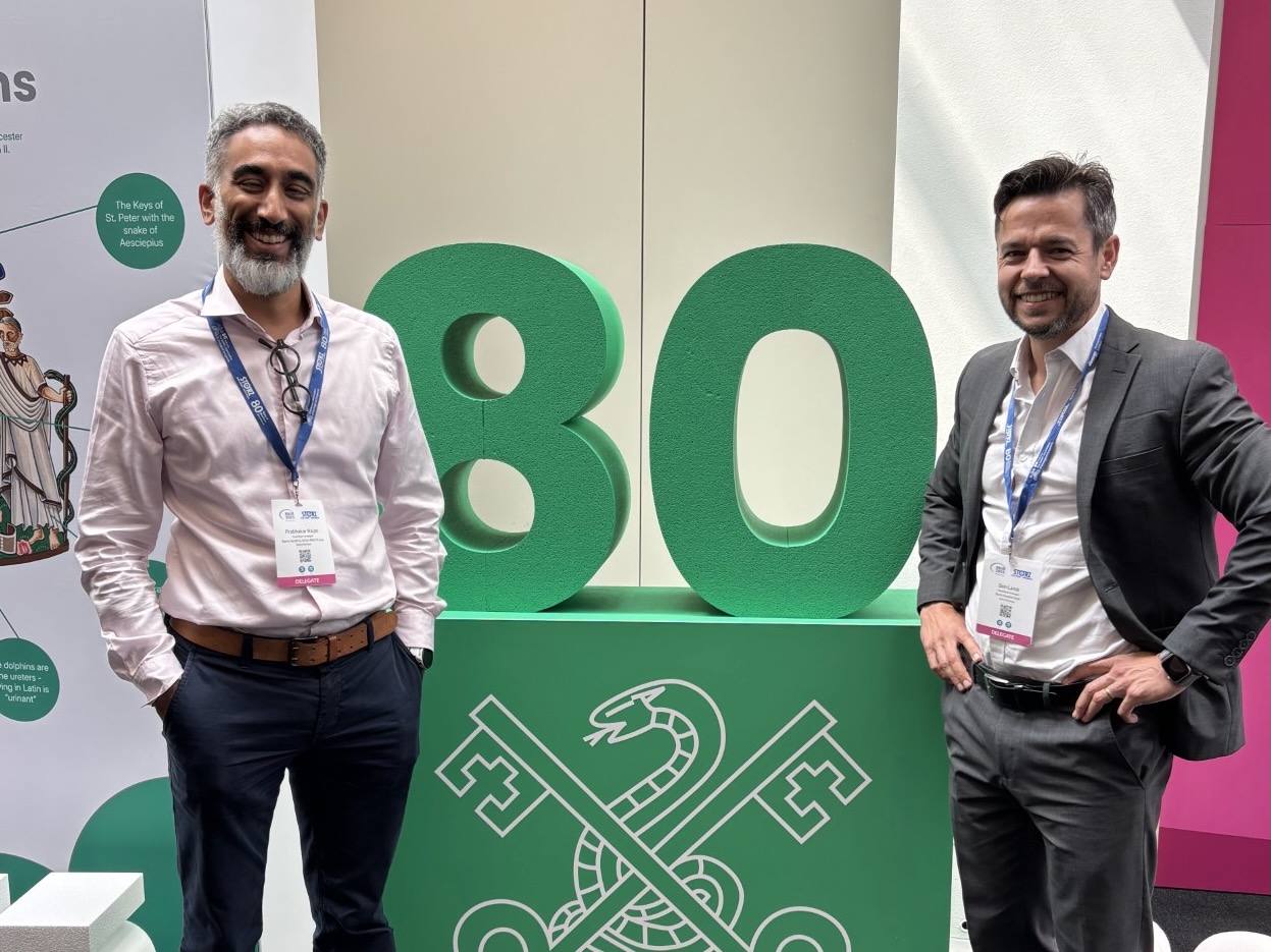 Two men are standing either side of a green table which has the number 80 on top of it.