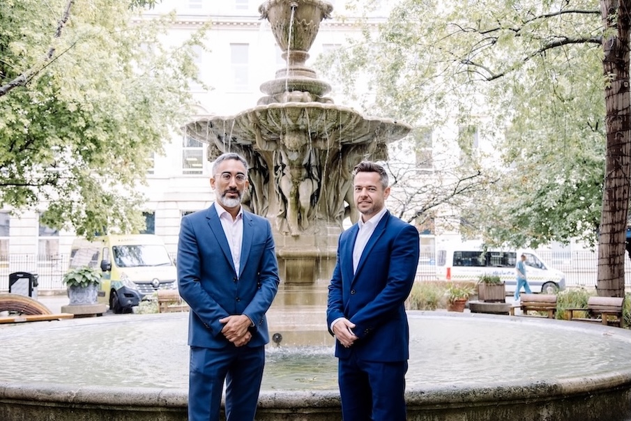 Two men in suits are standing in front of a fountain.