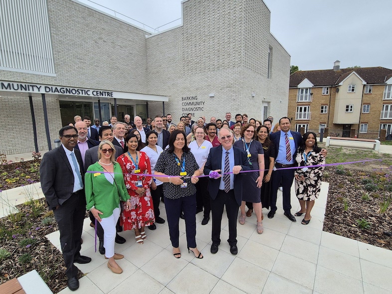 A group of people are standing outside a hospital for a ribbon cutting opening event