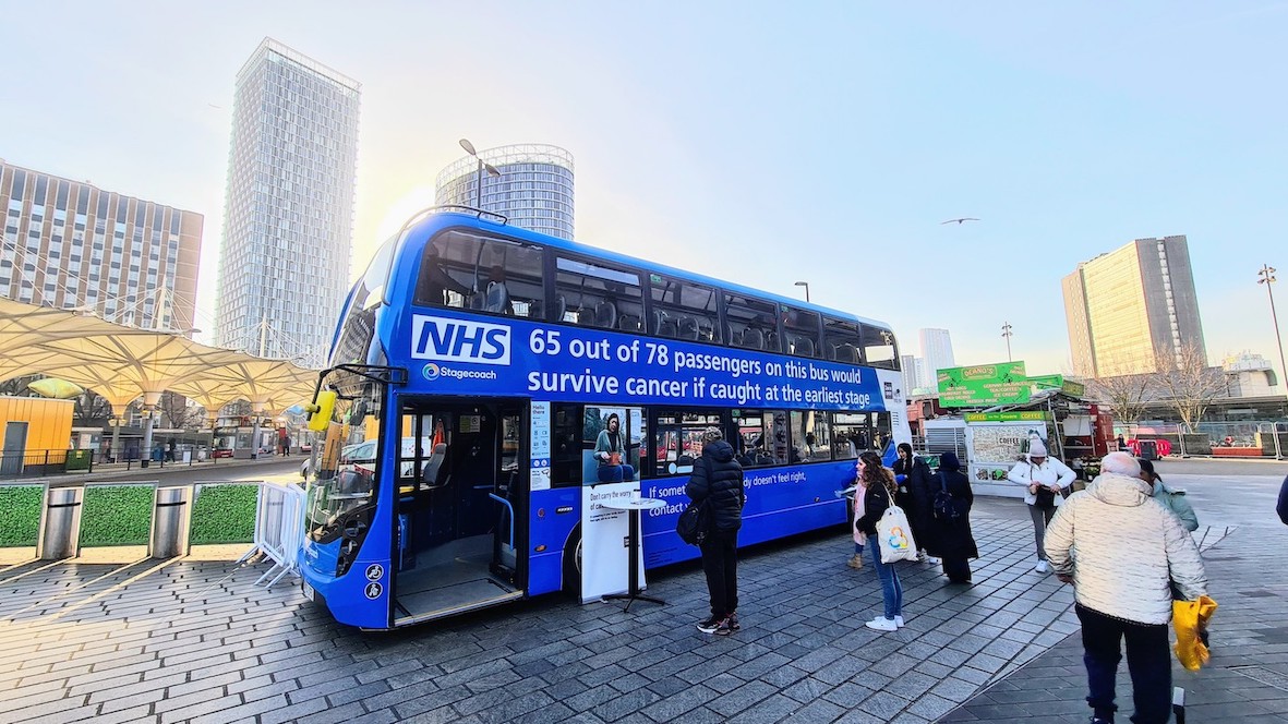 People are walking in front of a blue double-decker NHS bus.