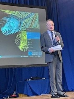 A man in a grey suit is standing on a stage giving a presentation