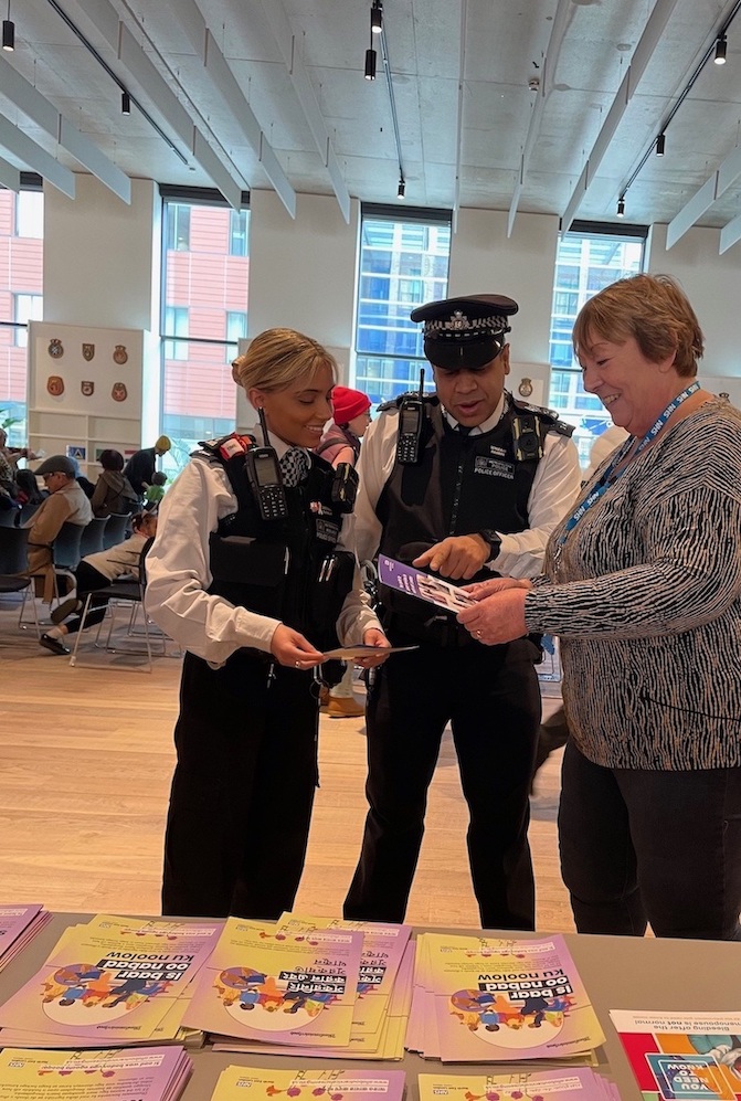 A lady is talking to two police officers and handing them information about cancer signs and symptoms