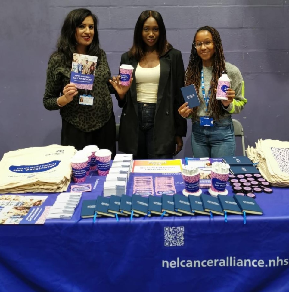 Three women are standing behind a table with HPV information leaflets on it.