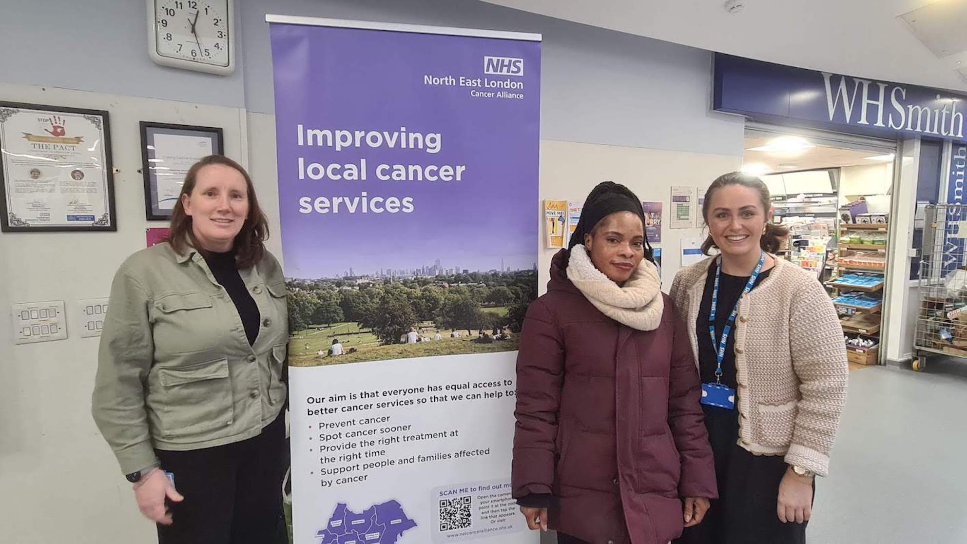 Three ladies are standing by a pop-up banner which says 'Improving local cancer services' on it