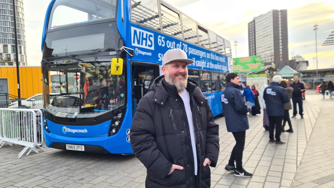 A man is standing in front of a blue double-decker NHS bus