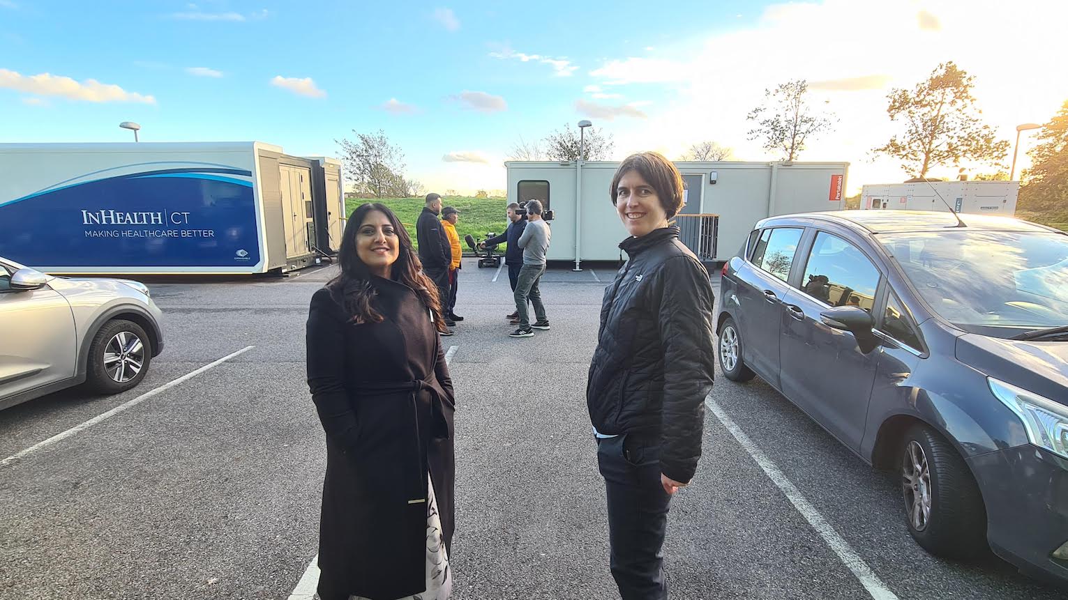 Two people standing in a car park in front of a lung scanning truck.