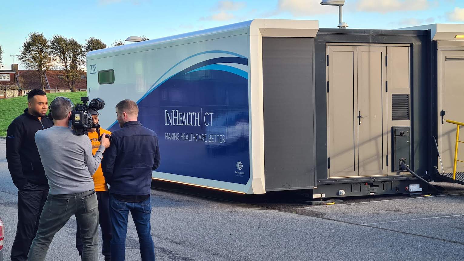 Two people standing in front of a lung scanning truck and being filmed by two other people.