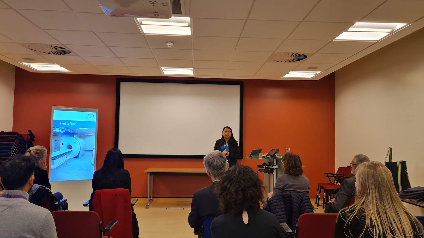 A person is giving a presentation in front of an audience who are seated inside a training room