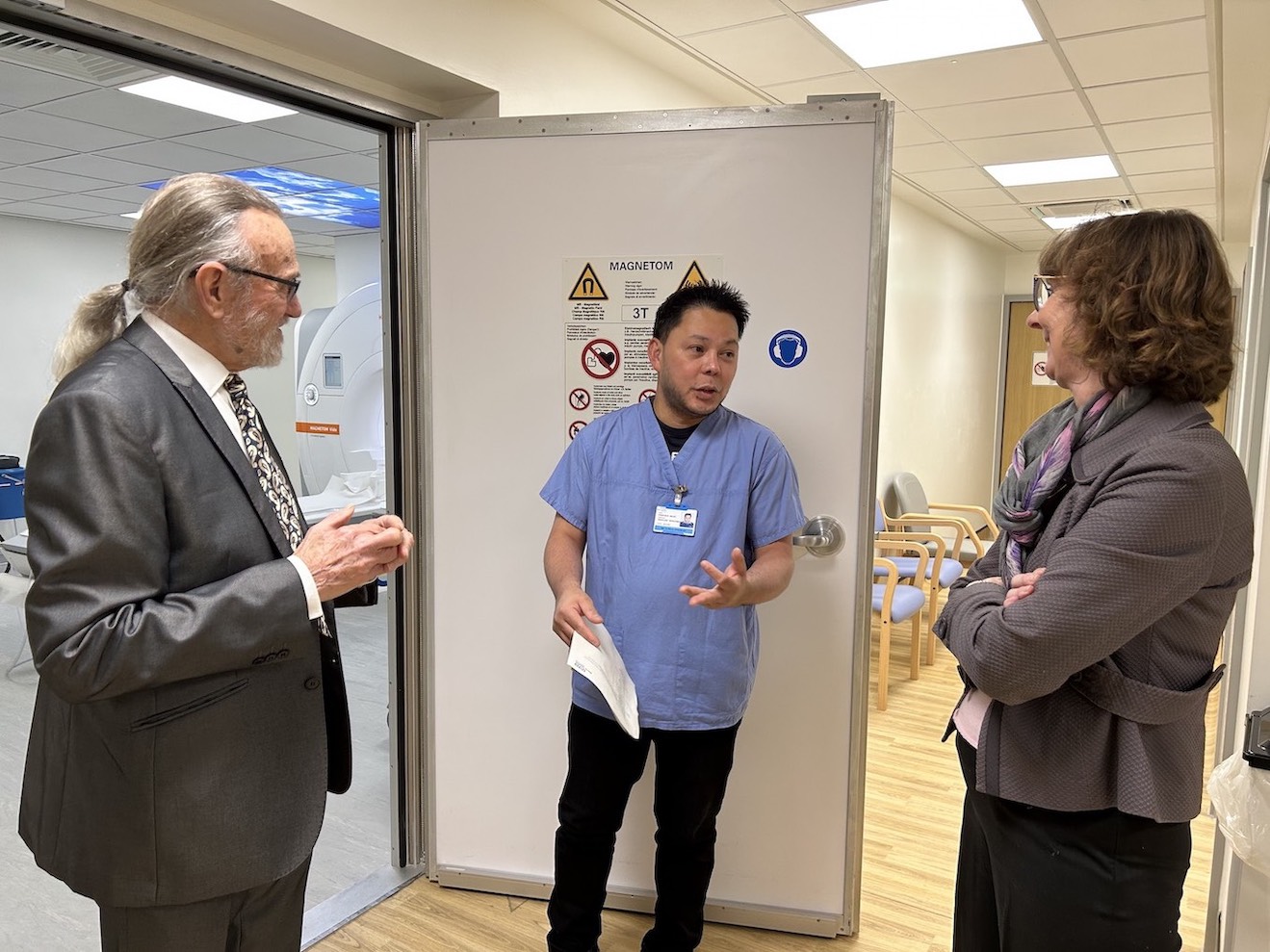 Three people are standing outside the entrance to an MRI scanner at a hospital