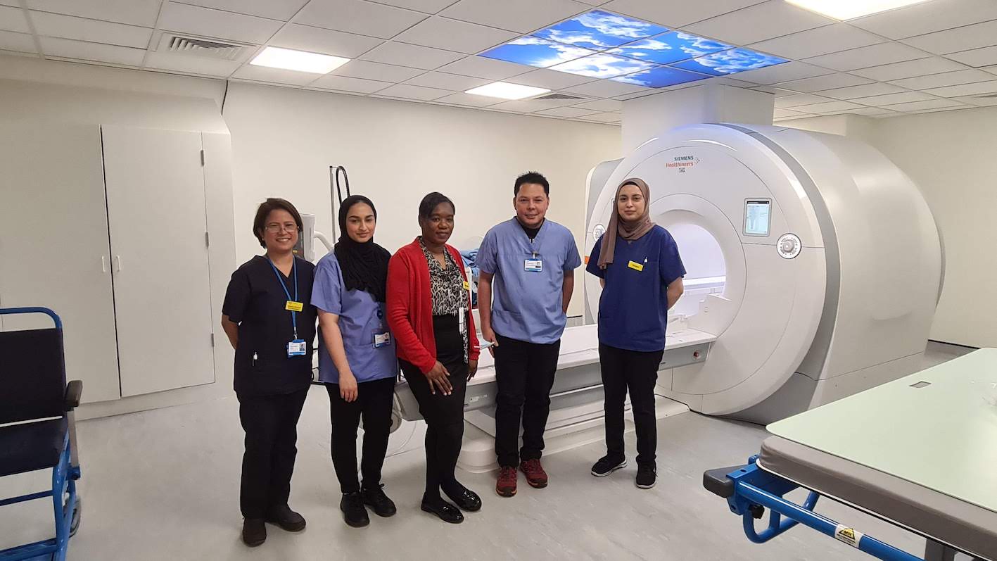 Five people are standing in front of an MRI scanner in a hospital