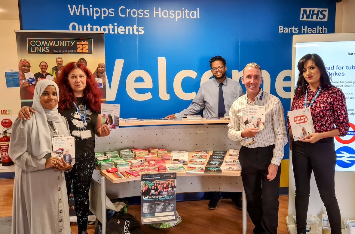 A group of people are standing in front of a table with cancer information leaflets on it.