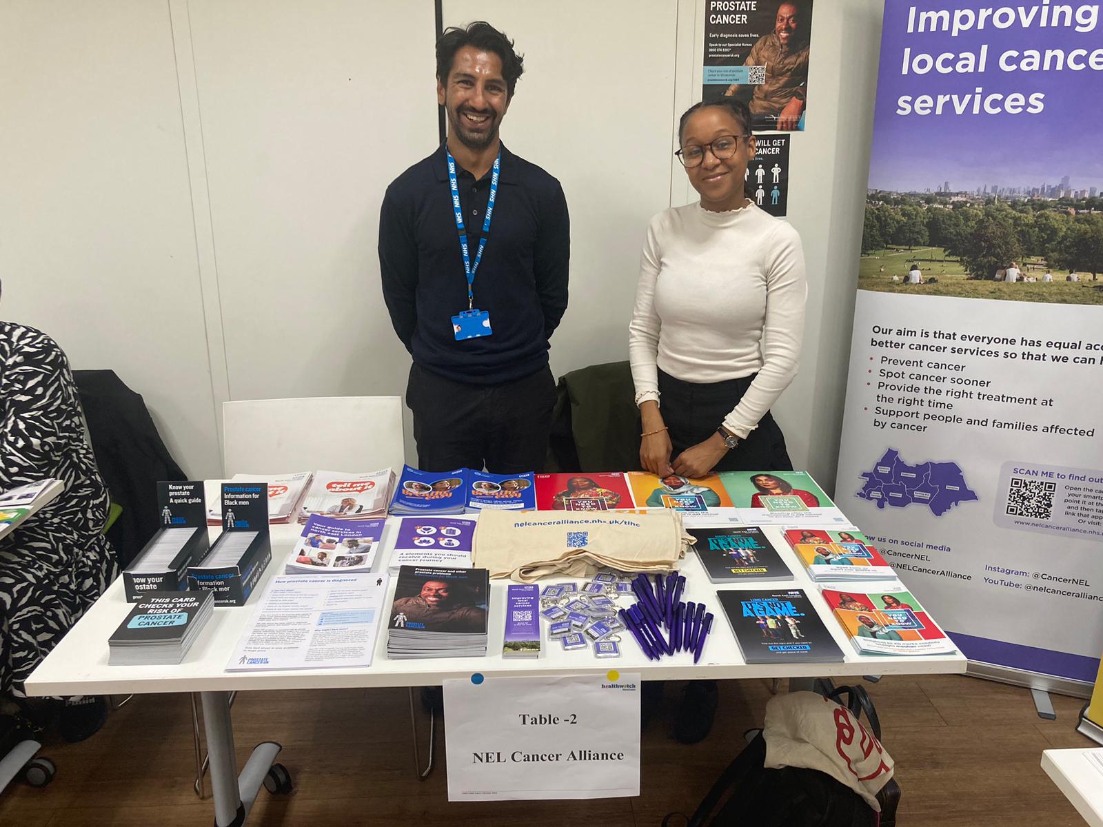 Two people are standing behind a table with cancer information on it