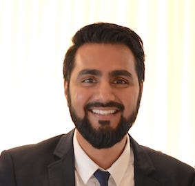 An asian man wearing glasses and a suit is looking towards the camera