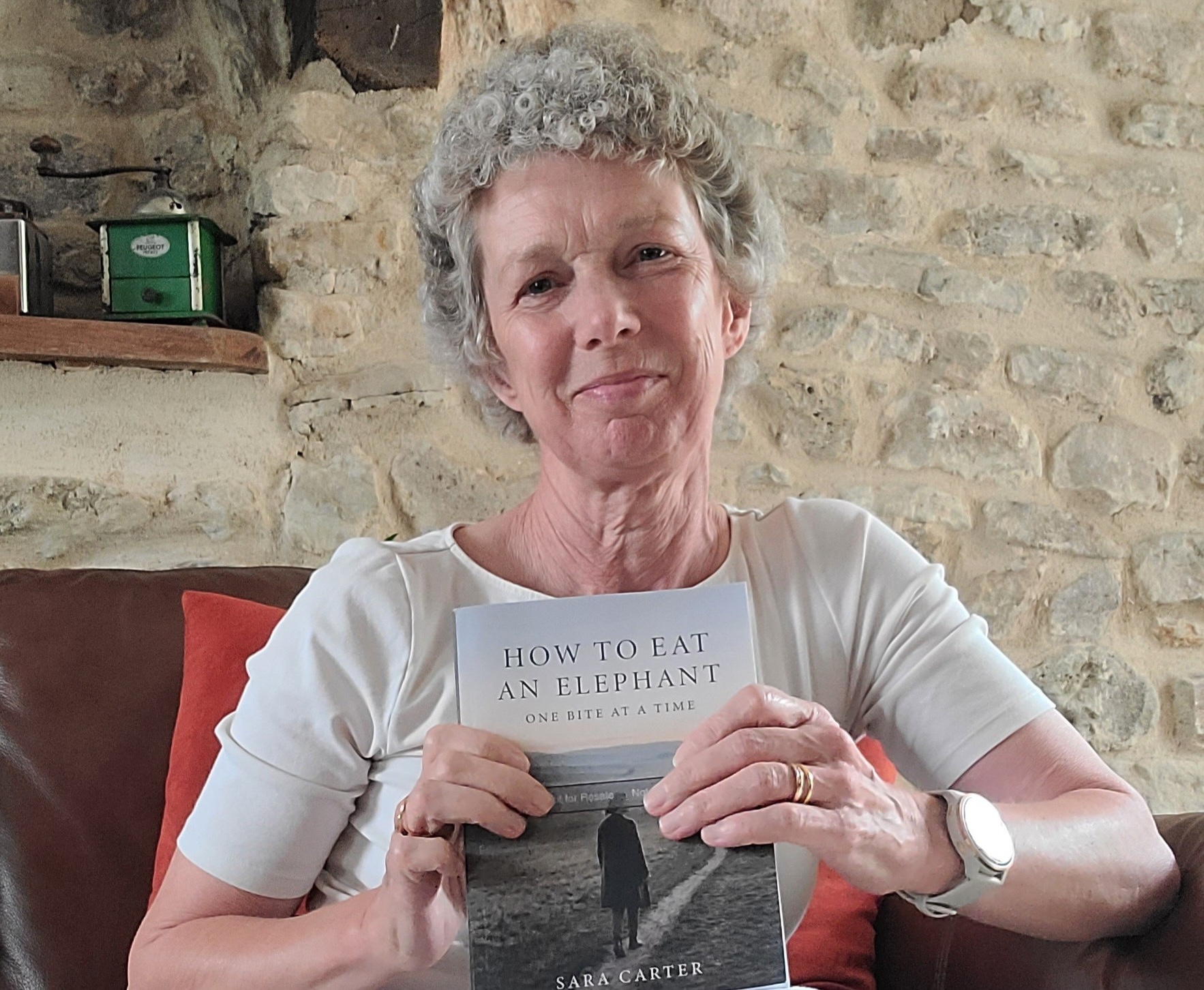 A lady is sat down holding a book which is called How to eat an elephant one bite at a time
