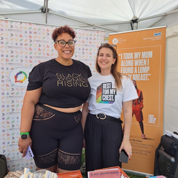 Two people are standing in front of a marketing information stand. One one T-shirt it says Black Women Rising and on the other it says Best For My Chest
