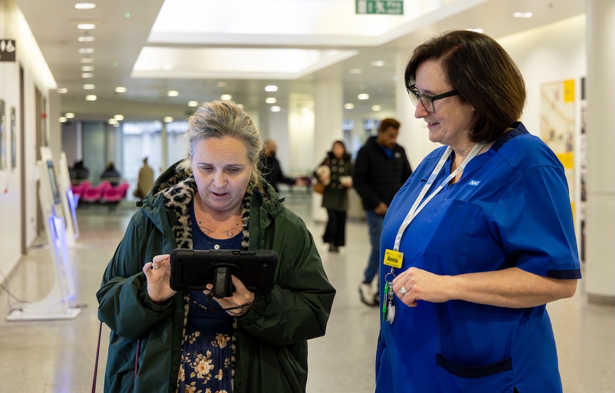 A nurse is talking to a patient who is looking at an interactive digital device.