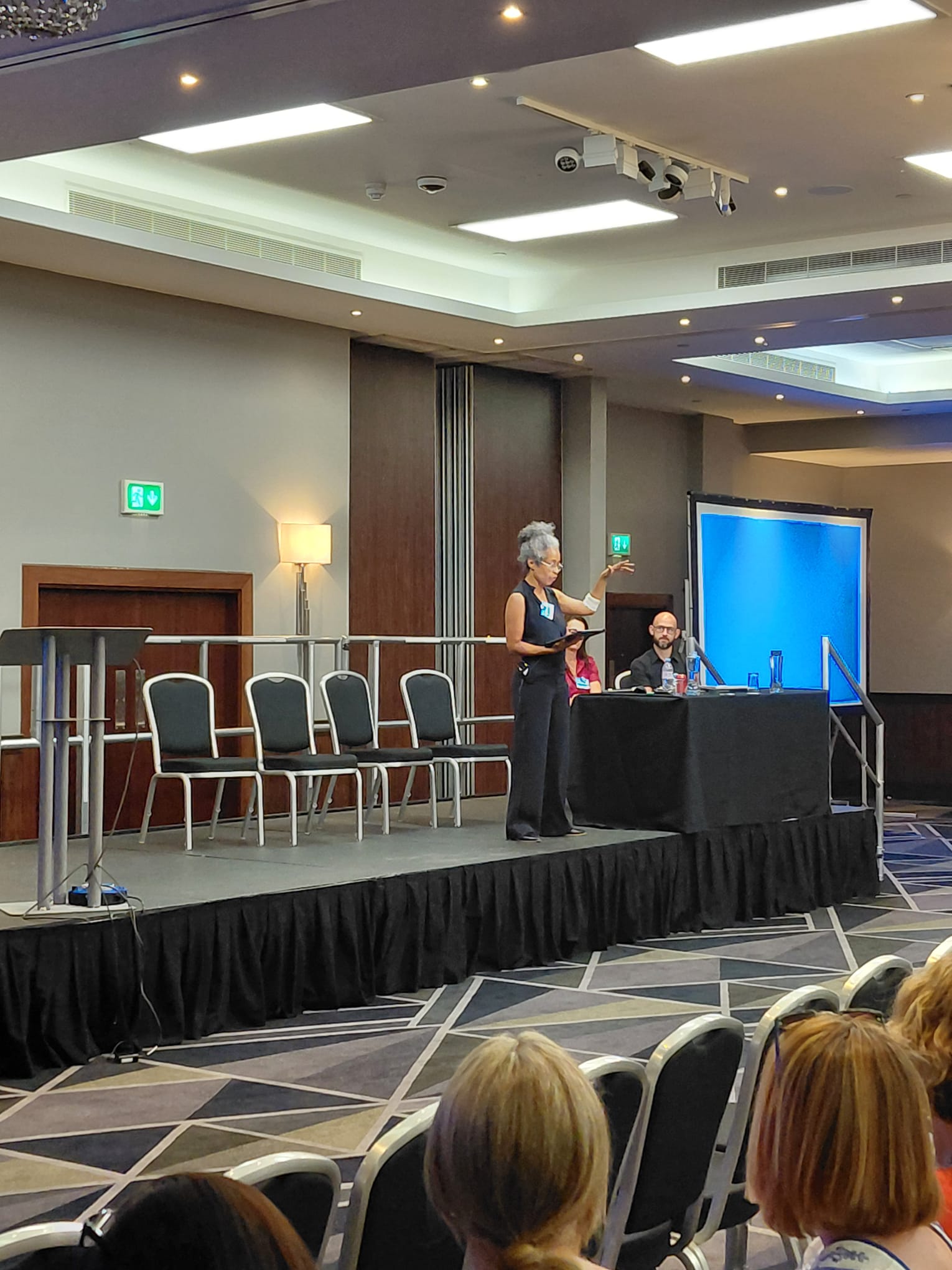A lady is presenting on a stage to a large audience.