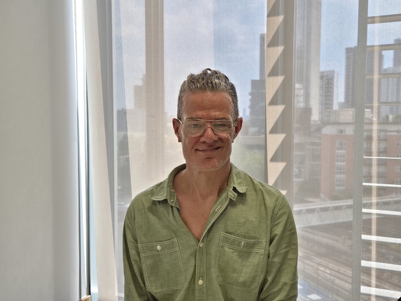 A man wearing a green shirt and glasses is sitting in an office