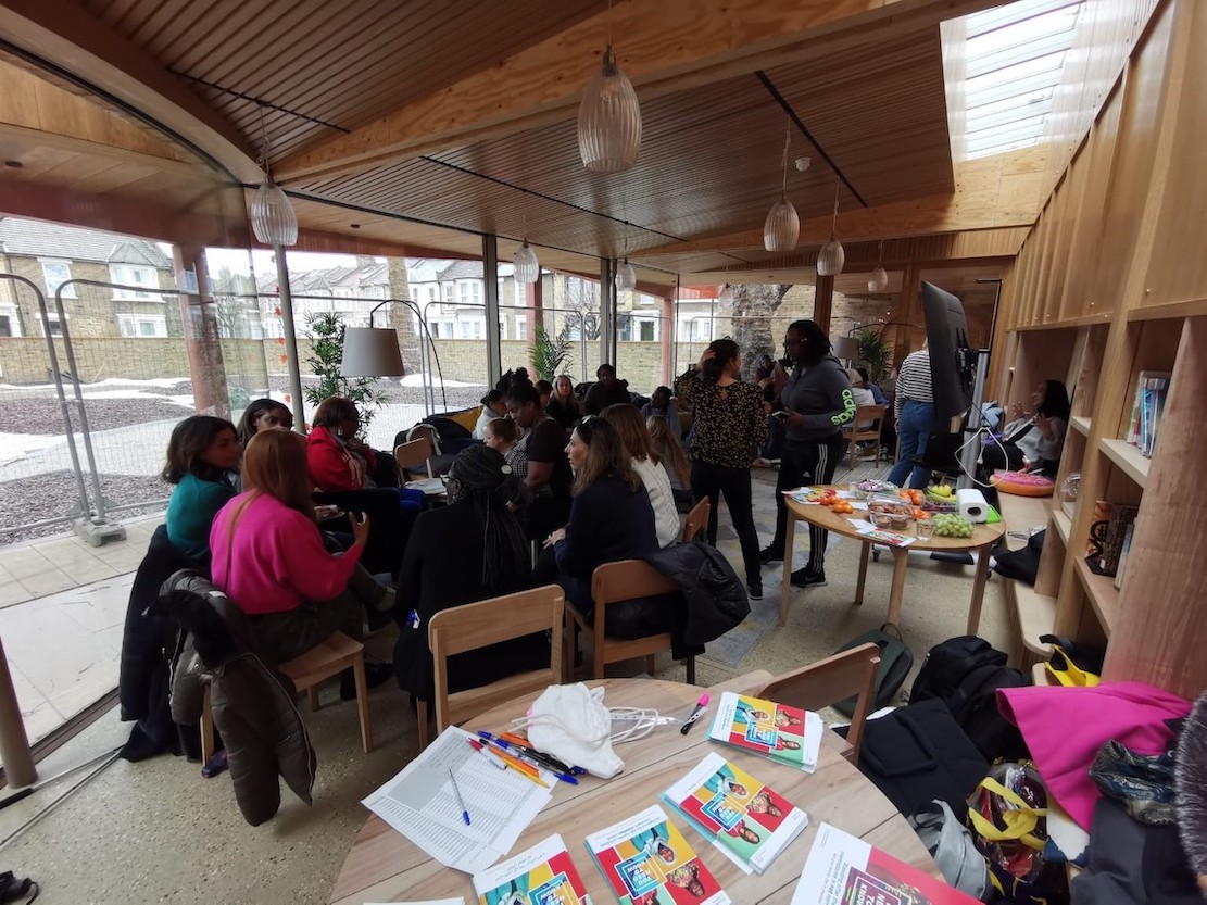 The images shows a room full of people sat in discussion groups at some tables.