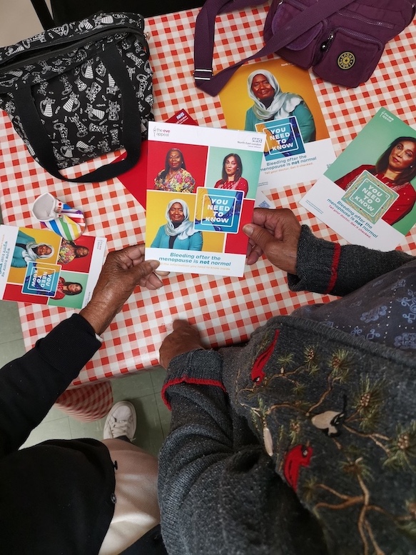 Two people are holding a leaflet above a table. You can just see their hands holding the leaflet.  On the leaflet it says You Need To Know