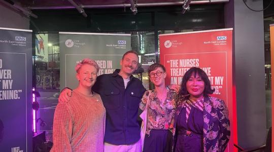 A group of four people standing in front of some banners and smiling at the audience.