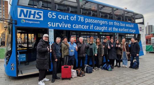 A group of people are standing in front of a blue double-decker NHS bus