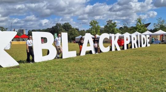 Large letters in a park spell out Black Pride against a sunny and cloudy sky