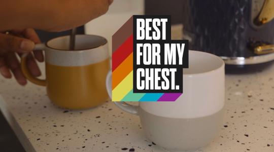 The image is of two coffee cups on a kitchen work surface. The words Best For My Chest appear in the centre in white bold text with rainbow colours shooting out to the left. 