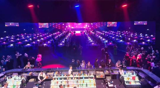 The image is off a venue for an awards ceremony showing all the tables laid out and the bar before guests have arrived. The lighting is ambient with colours of blue and purple.