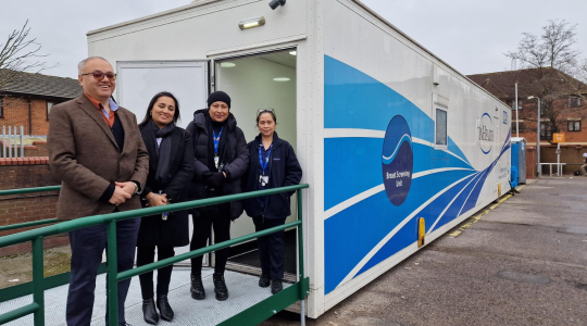 Four people are standing in front of a breast screening truck