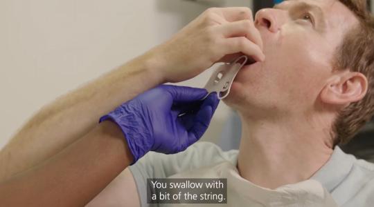 A man is swallowing a pill and a nurse's hand is holding on to some string which is attached to the pill