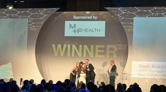 A group of people are on stage receiving an award in front of an audience and a sign says winner behind the stage