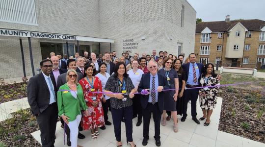 A crowd of people are outside a hospital for a ribbon cutting opening event