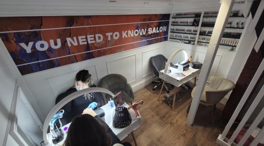 The image is of the inside of a nail salon with a lady having her nails done. On the wall is a banner which sat You Need To Know Salon on it