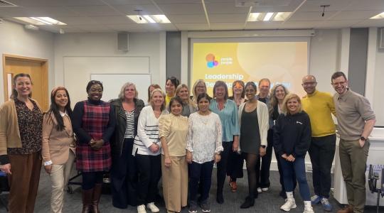 A large group of people is standing together for a team photo in a large meeting room with a presentation screen behind them