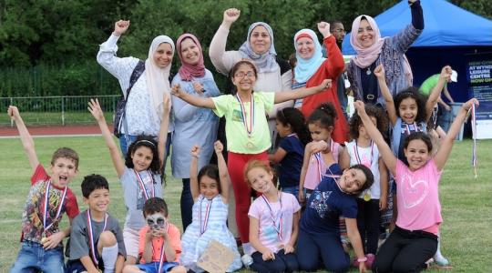 A large group of women and children are wearing medals and celebrating with their hands in the air.