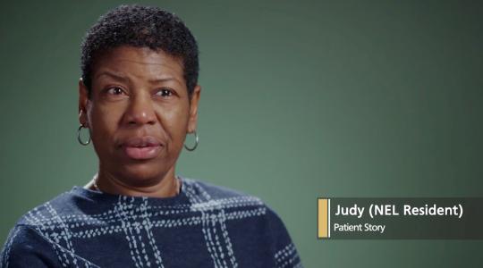 A lady is facing the camera against a dark green background. A caption says Judy (NEL resident) Patient Story.