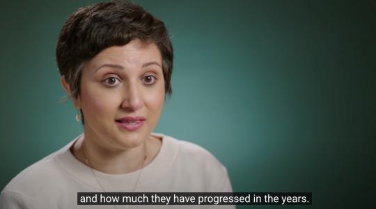 A lady is facing the camera with a dark green background behind her. A caption below her says and how much they have progress in the years.