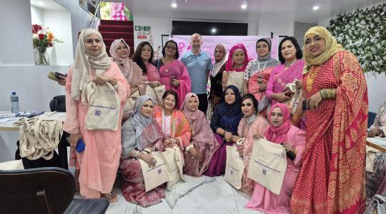 A man in a blue shirt in in the middle of a large group of asian ladies wearing pink outfits