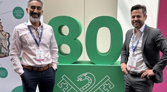 Two men are standing either side of a green table which has the number 80 on top of it.
