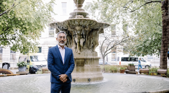 A man in a suit is standing in front of a fountain.