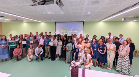 A large group of people in a meeting room are standing together for a photo.