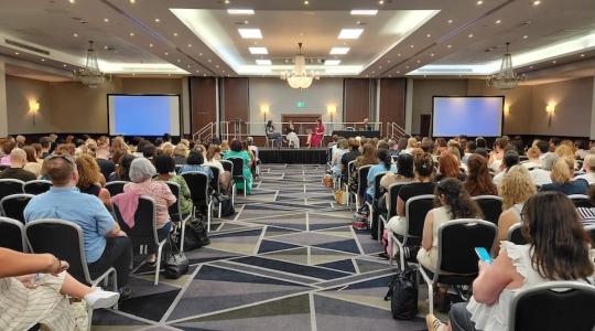 A conference hall with an audience sat in chairs facing the front.